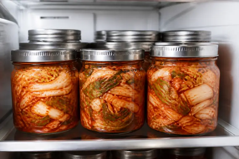 Mehrere Gläser mit fermentiertem veganem Kimchi sind ordentlich im Kühlschrank nebeneinander aufgereiht, bereit zur Lagerung.