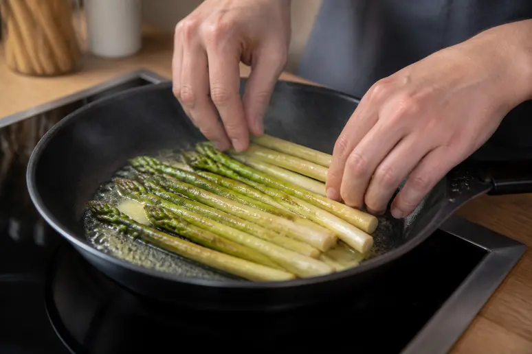Gekochter Spargel wird sorgfältig in einer Pfanne mit Butter erwärmt, um ihn sicher und schmackhaft für den erneuten Verzehr vorzubereiten.