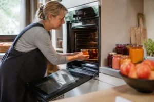 Frau schichtet Gläser mit Obst zum Einkochen im Backofen ein, praktische Konservierungsmethode.