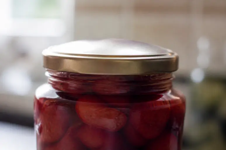 Aufgeblähter Deckel bei einem Glas mit eingekochten Erdbeeren als Warnzeichen für Verderb.