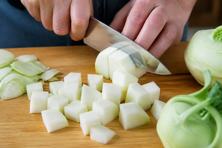 Hände schneiden sorgfältig Kohlrabi für das sichere Einkochen in mundgerechte Stücke.