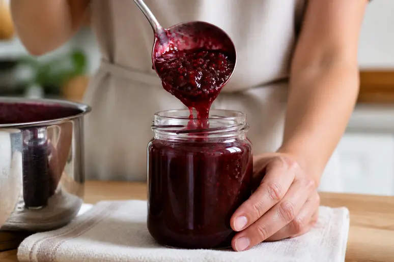 Hände füllen ein sterilisiertes Glas mit heißem Preiselbeermus beim Preiselbeeren einkochen.
